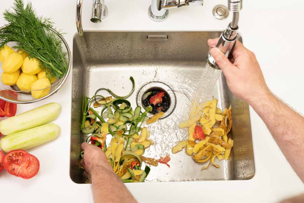 homeowner rinsing food scraps down the kitchen drain